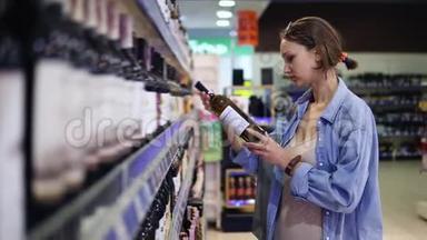 一个在酒精部门超市的女人。 酒架。 女孩选一瓶，拿一瓶酒.. 看上去